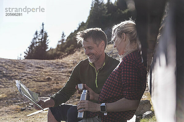 Happy couple reading newspaper and sitting on mountain in Tyrol