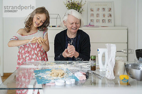 Smiling girl kneading dough for cookies with grandmother