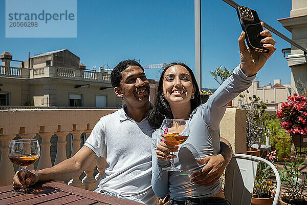 Happy young woman taking selfie with boyfriend at terrace on sunny day