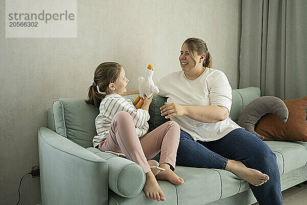 Mother and daughter playing with stuffed toy sitting on sofa at home