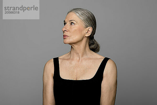 Confident senior woman in black sportswear looking away against gray background