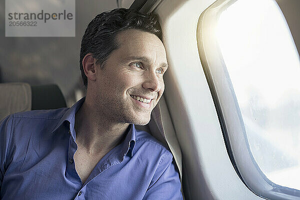 Smiling handsome businessman looking out through airplane window