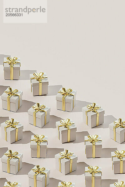 Repetition of gift boxes wrapped in golden ribbon over colored background