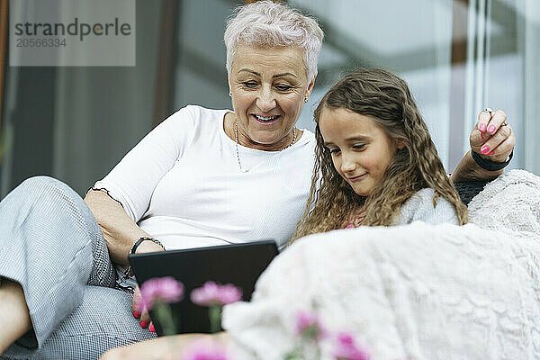 Happy senior woman using tablet PC with cute granddaughter at patio