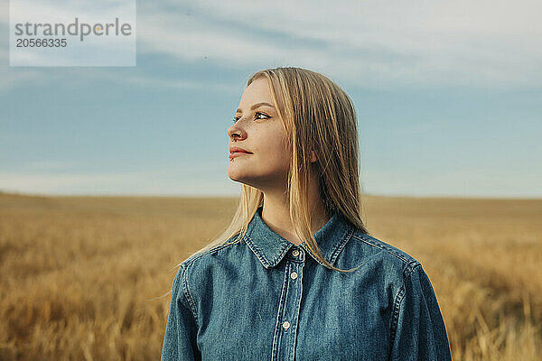 Thoughtful young woman in denim shirt at wheat field