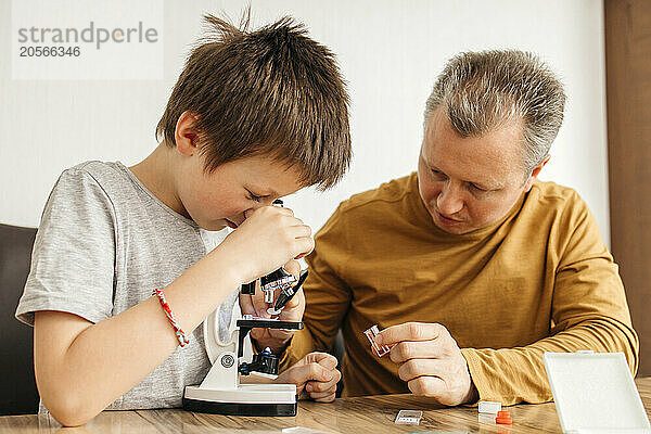 Boy looking through microscope and father assisting at home