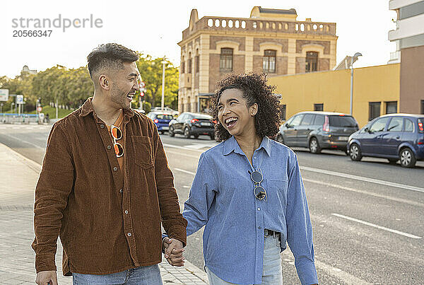 Happy young couple holding hands and walking on street