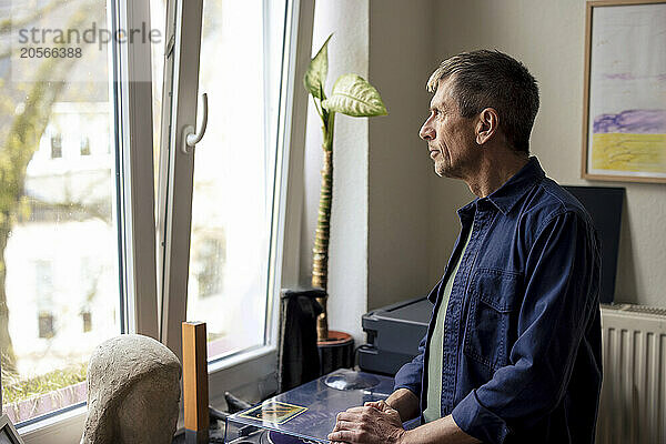 Thoughtful senior man looking out through window at home