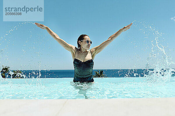 Mature woman splashing water and having fun in swimming pool at resort