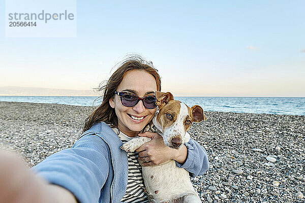 Happy woman taking selfie with Jack Russell Terrier at beach in Sicily