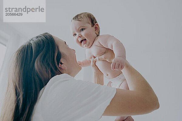 Happy young mother holding baby boy aloft at home