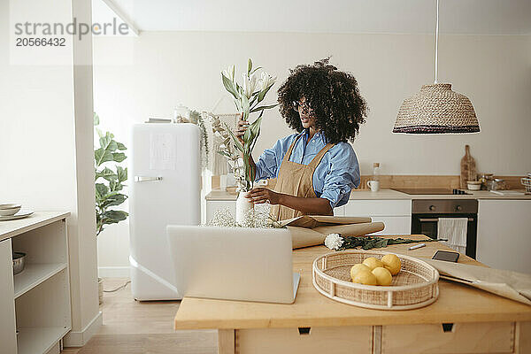 Woman putting flowers in vase at kitchen workspace