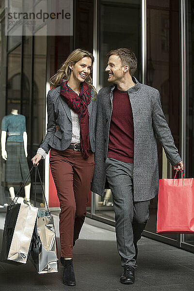 Happy boyfriend and girlfriend carrying shopping bags and walking on street