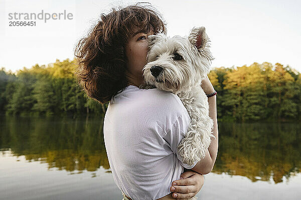 Girl embracing and kissing white dog near river