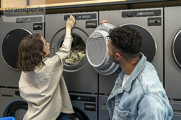 Young woman operating dryer by boyfriend in laundromat