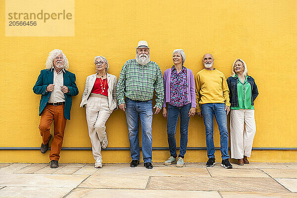 Fashionable elderly friends leaning on yellow wall