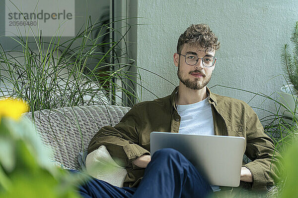 Handsome young man sitting with laptop in balcony