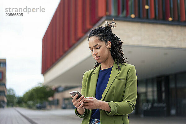 Beautiful young businesswoman using smart phone standing at office park