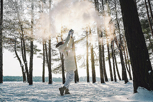 Woman throwing snow standing amidst trees in winter forest