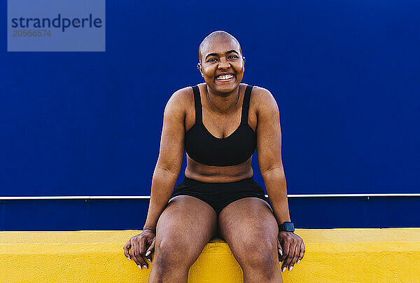 Happy bald woman sitting in front of blue wall