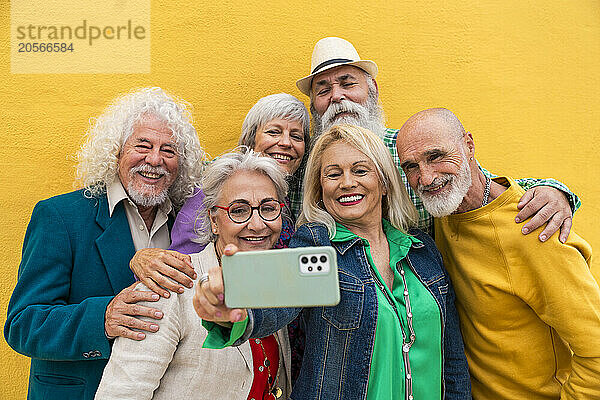 Happy senior woman taking selfie with friends in front of yellow wall