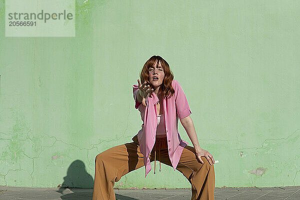 Confident beautiful redhead woman dancing in front of mint green wall on sunny day