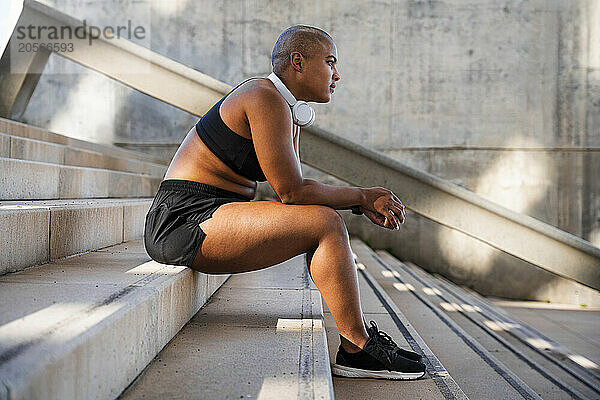 Confident sporty woman with headphones sitting on steps