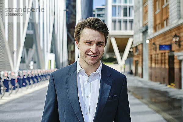 Smiling businessman standing on street near buildings