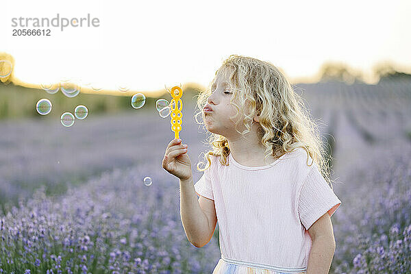 Cute girl blowing bubbles and standing in lavender field