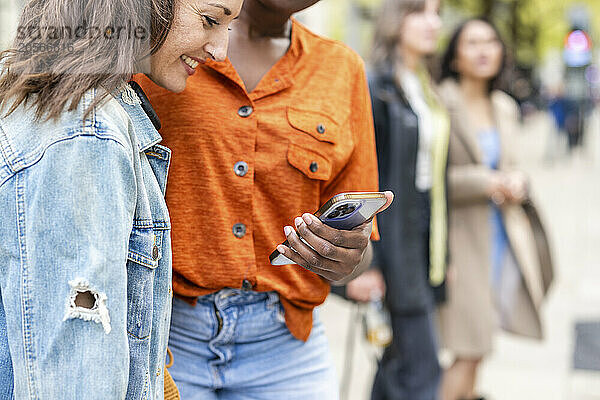 Woman sharing smart phone with smiling friend