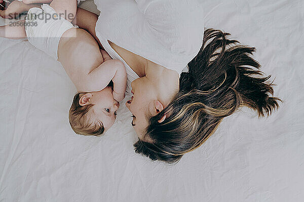 Happy mother spending leisure time by lying on bed with baby boy at home