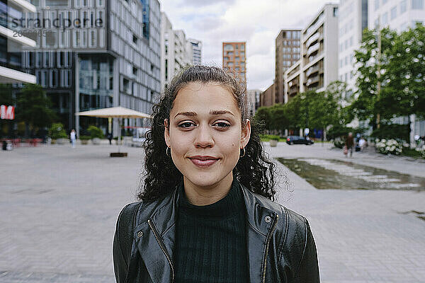 Beautiful young woman wearing black leather jacket in city