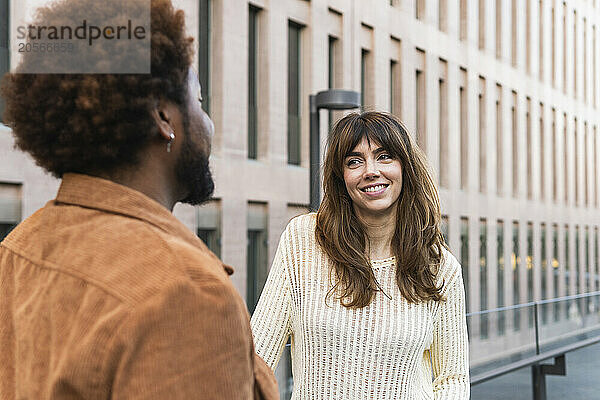 Smiling woman and man talking in front of modern building