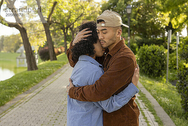 Young man embracing girlfriend and standing at park