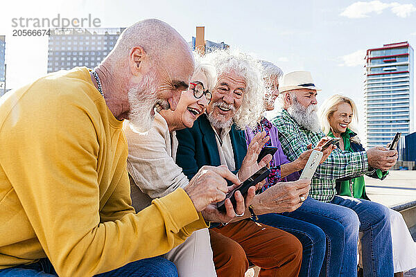 Happy men and women using smart phones sitting together