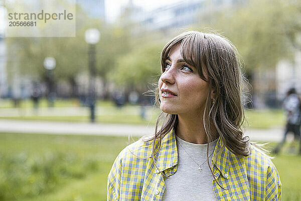 Beautiful young woman wearing checked pattern shirt looking away at park