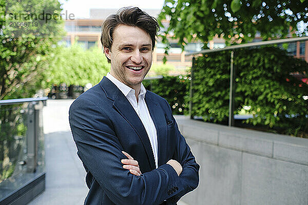 Happy businessman standing with arms crossed in office park