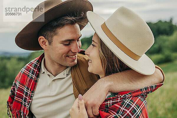 Smiling man with arm around girlfriend in plaid shawl on meadow