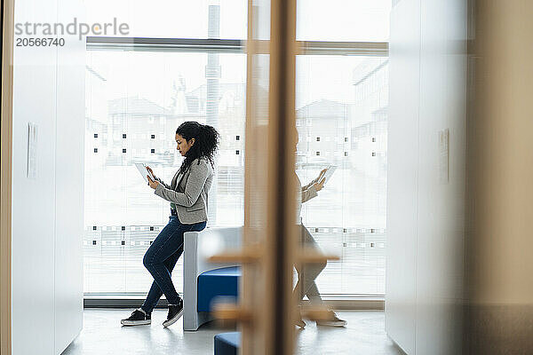 Businesswoman using tablet PC and leaning on chair at office