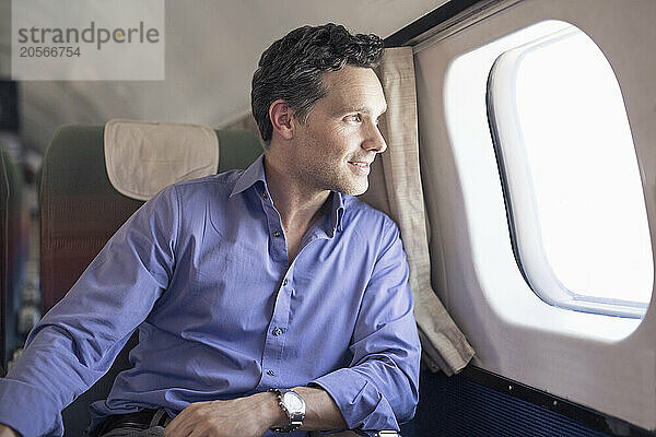 Smiling mature businessman looking out through airplane window