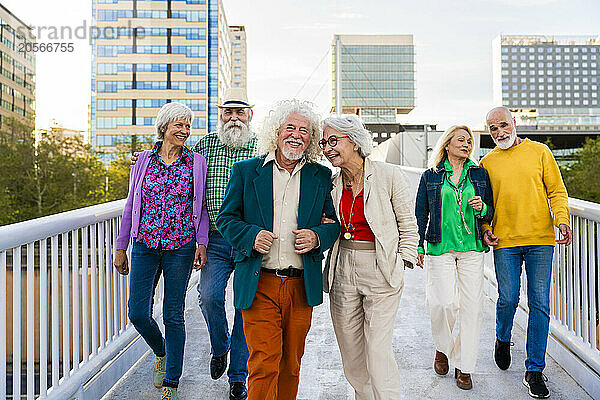 Smiling retired men and women walking together on footbridge in city