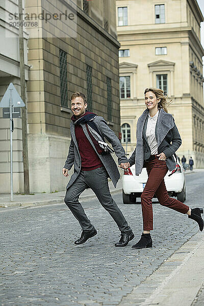 Boyfriend and girlfriend holding hands and crossing street in city