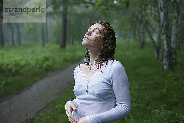 Carefree woman with eyes closed enjoying rain in forest