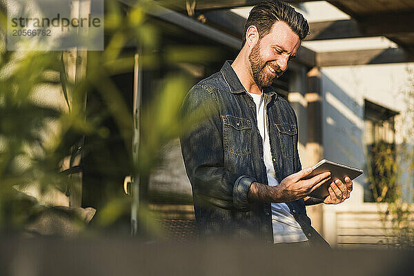 Happy man with beard using tablet PC on sunny day