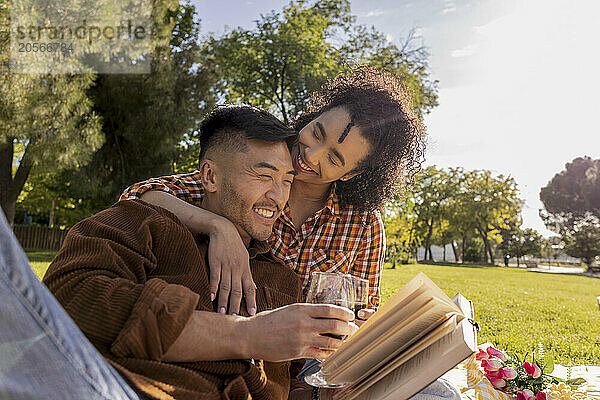 Happy man reading book and leaning on girlfriend at public park