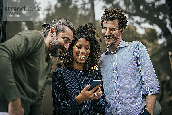 Laughing coworkers using smartphone on sunny day