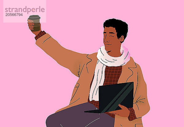 Smiling man holding disposable coffee cup sitting with laptop in front of pink background