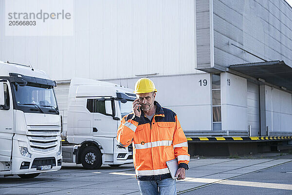 Confident mature manager wearing protective workwear talking on mobile phone at warehouse