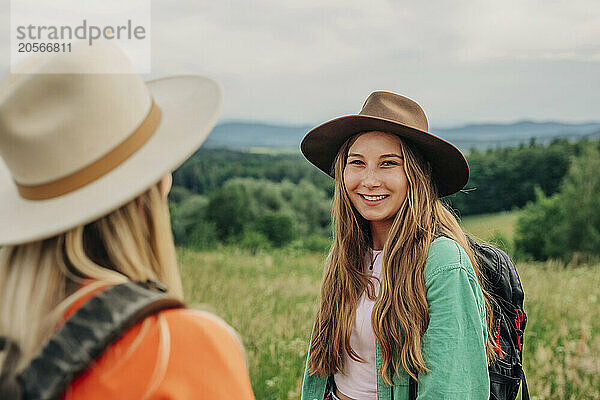 Happy woman wearing hat and backpack with friend on mountain