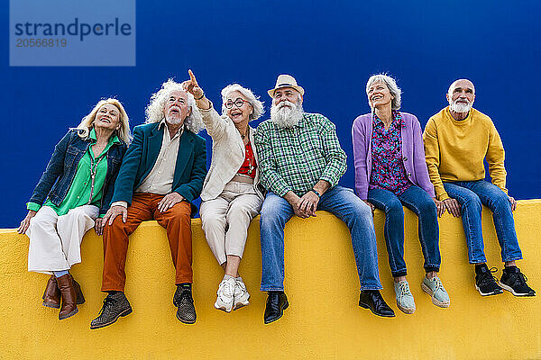 Cheerful senior friends sitting on yellow wall